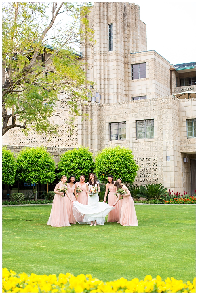 bride in matthew christopher wedding dress with cap sleeves with white, pink and orange ranunculus flowers and greenery bouquet with bridesmaids in blush wedding dresses getting ready on wedding day in front of Arizona Biltmore