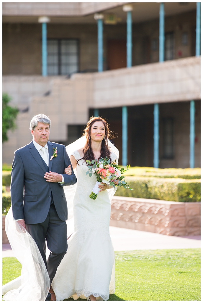 bride in matthew christopher wedding dress with cap sleeves with white, pink and orange ranunculus flowers and greenery bouquet walking down aisle with father at wedding ceremony
