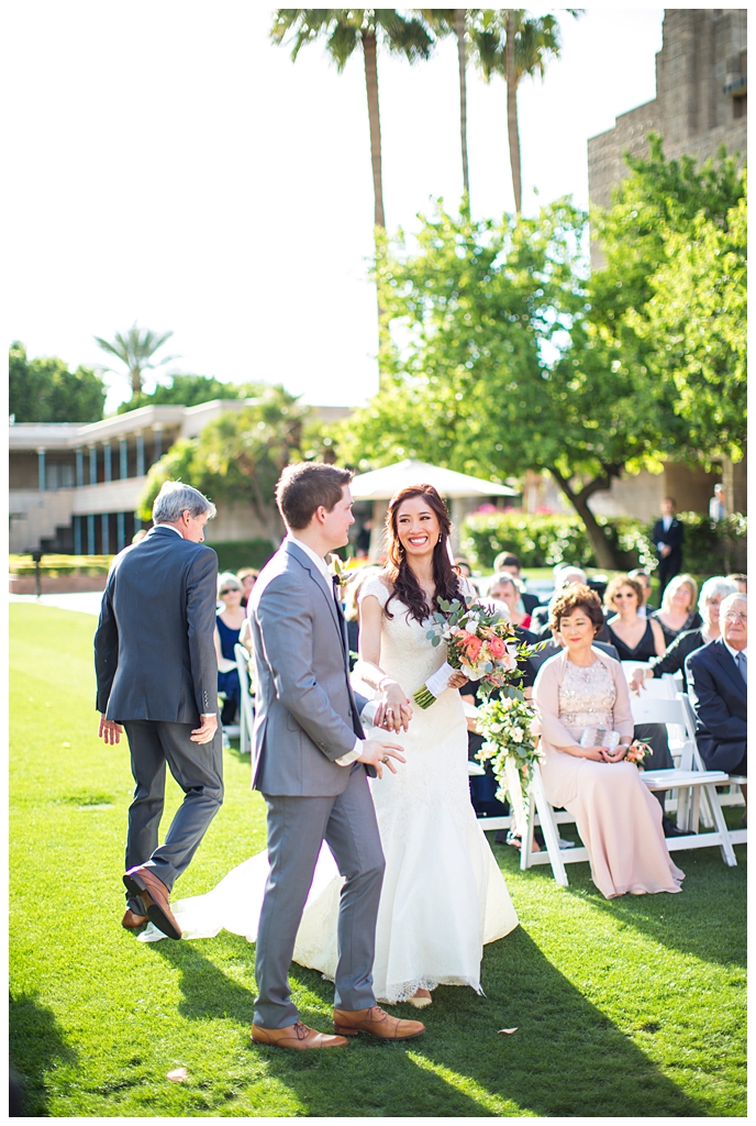 bride in matthew christopher wedding dress with cap sleeves with white, pink and orange ranunculus flowers and greenery bouquet with groom in light gray suit with tie wedding day ceremony at Arizona Biltmore