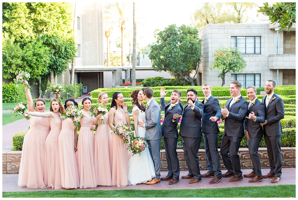 bride in matthew christopher wedding dress with cap sleeves with white, pink and orange ranunculus flowers and greenery bouquet with groom in light gray suit with tie with wedding party bridesmaids in blush dresses and groomsmen in dark gray suits wedding day portraits in Arizona biltmore garden