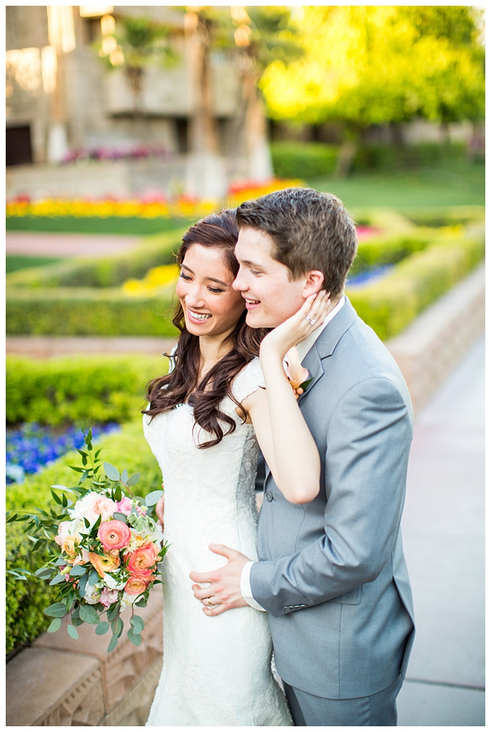 bride in matthew christopher wedding dress with cap sleeves with white, pink and orange ranunculus flowers and greenery bouquet with groom in light gray suit with tie wedding day portrait at Arizona Biltmore