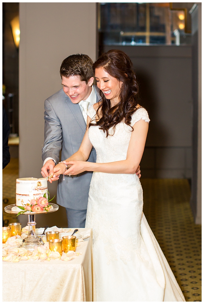 bride in matthew christopher wedding dress with cap sleeves with white, pink and orange ranunculus flowers and greenery bouquet with groom in light gray suit with tie wedding day cake cutting at Arizona Biltmore