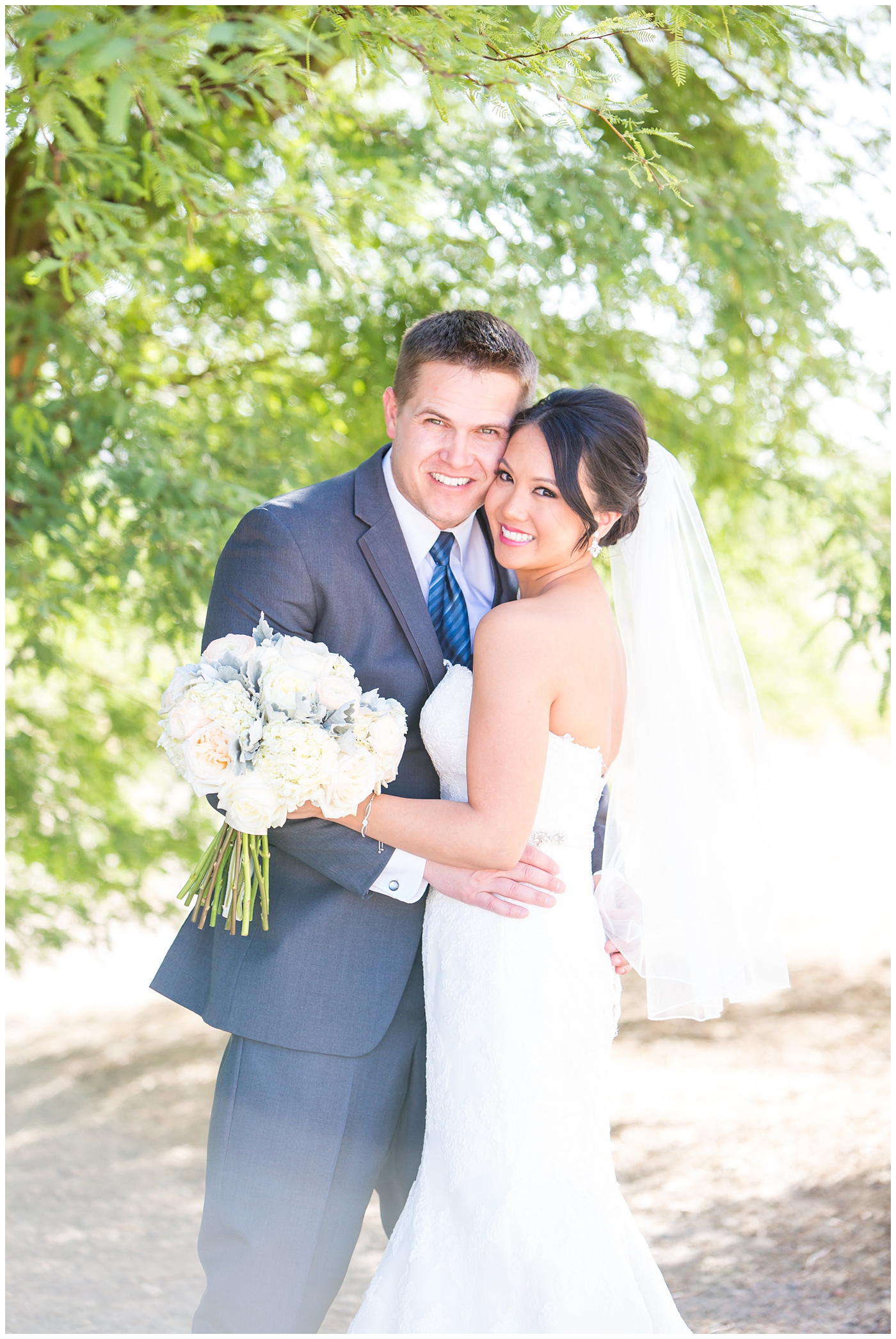 Bride in strapless maggie sorrento dress with soft white and pink roses bouquet with groom in light gray suit with blue tie and white rose boutonniere wedding day portrait