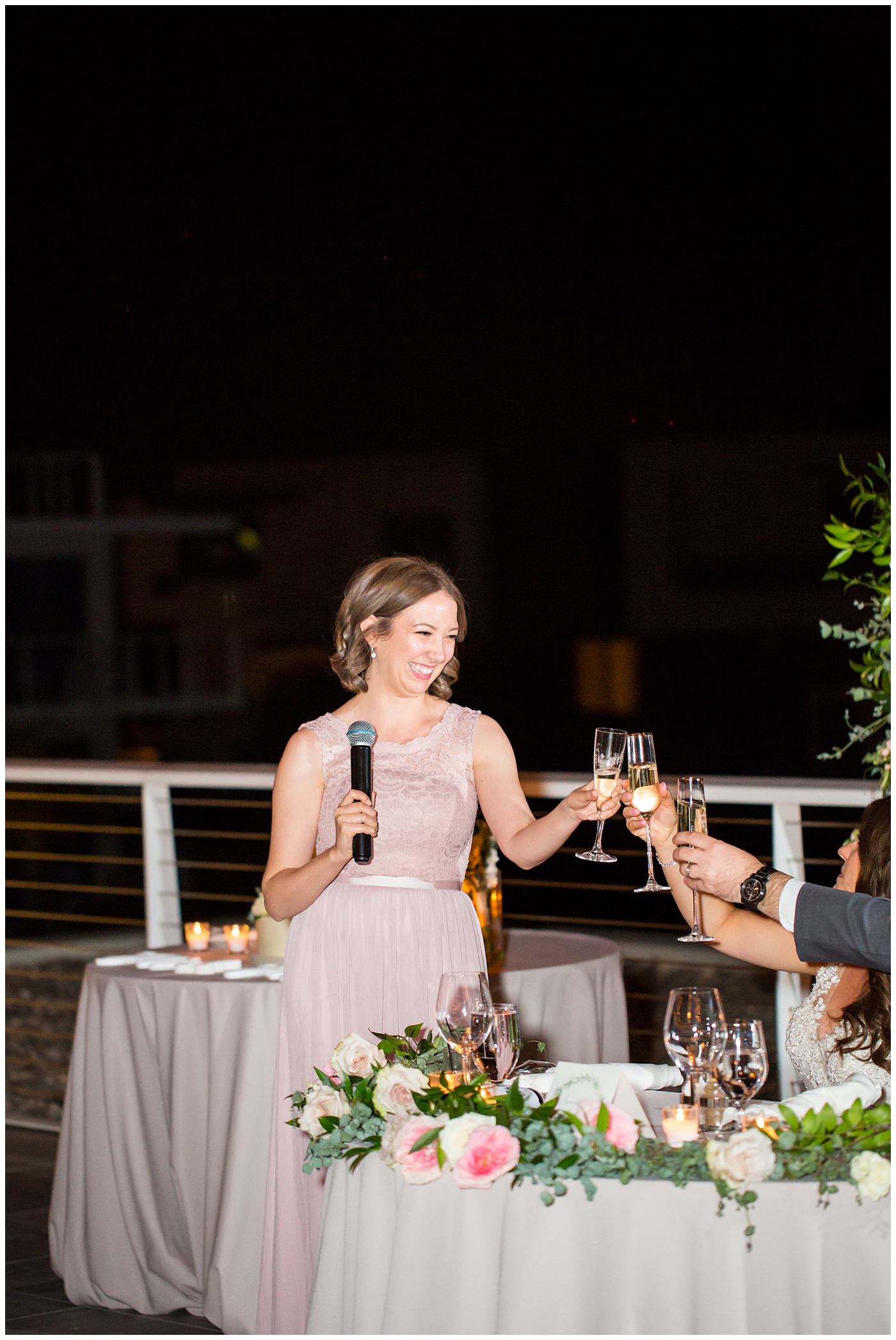 maid of honor giving speech with unique circle arch for outdoor rooftop wedding reception with wildflowers in blush and white with greenery with twinkle lights stranded above