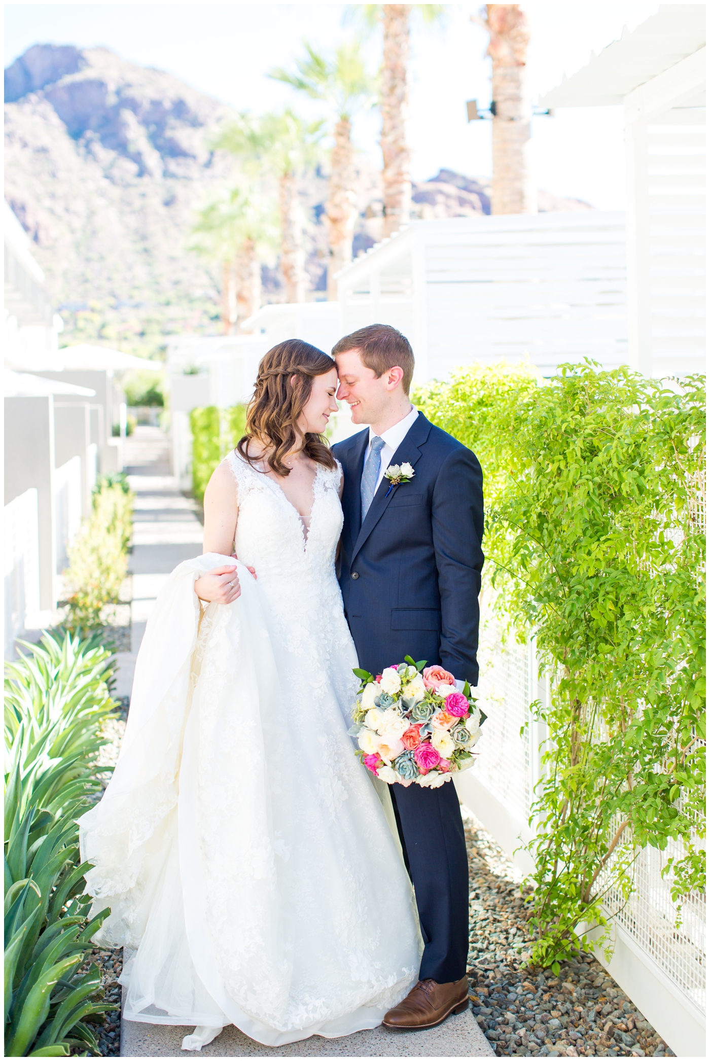 Bride in strapped deep v front and back Pronovias dress with bring pink peonies and succulents bouquet with groom in navy blue suite with succulent boutonniere wedding day portrait at mountain shadows